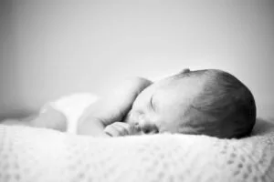 A serene black and white photo of a sleeping newborn baby wrapped in a soft blanket.
