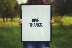 person holding rectangular black wooden photo frame with Give. Thanks. print
