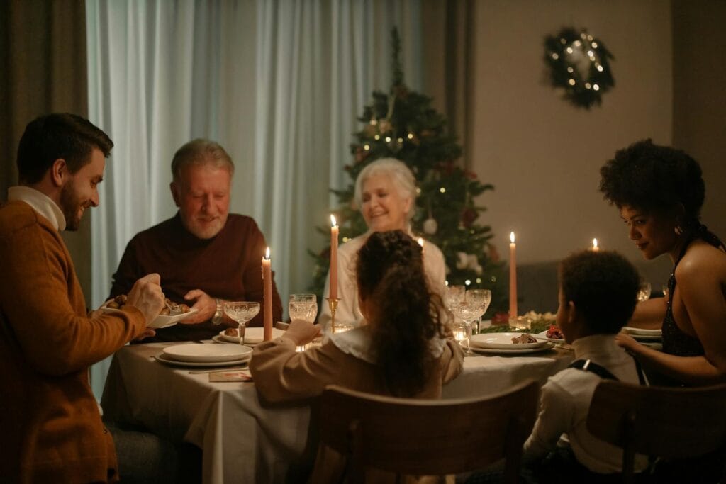 A joyful family enjoying a festive Christmas dinner together with candles and a Christmas tree indoors.