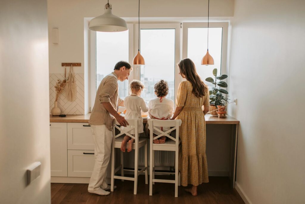 Family of four spending time together in a cozy kitchen setting, viewed from behind.