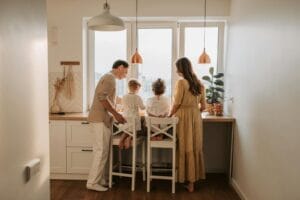 Family of four spending time together in a cozy kitchen setting, viewed from behind.