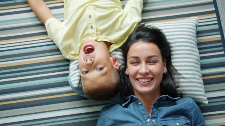 Mother and son lying on striped rug smiling